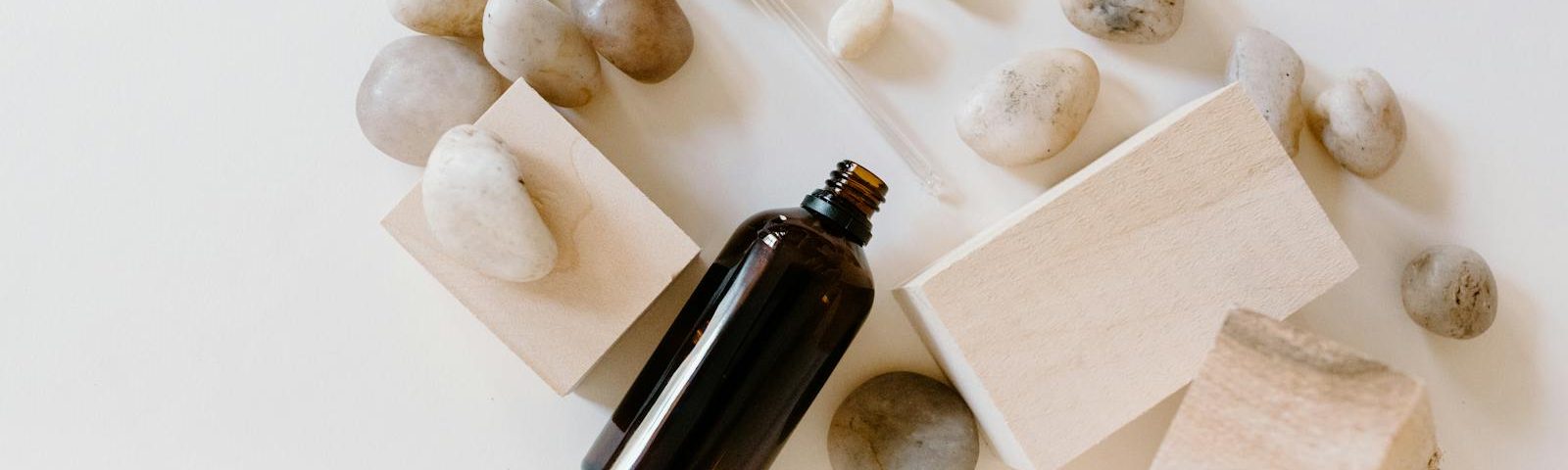 Flat lay of essential oil bottle with stones and wooden blocks, perfect for wellness themes.