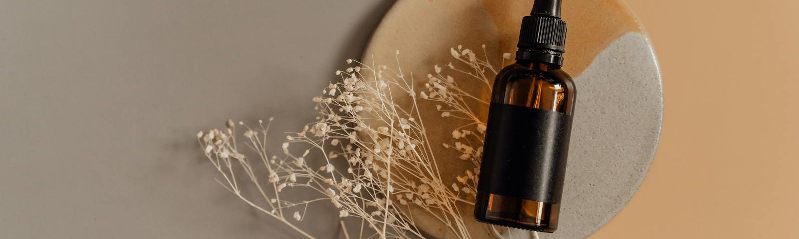 Aesthetic flatlay of a cosmetic dropper bottle on a minimalist background with dried flowers.