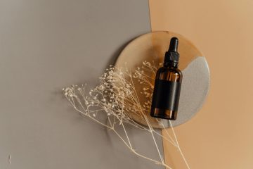 Aesthetic flatlay of a cosmetic dropper bottle on a minimalist background with dried flowers.